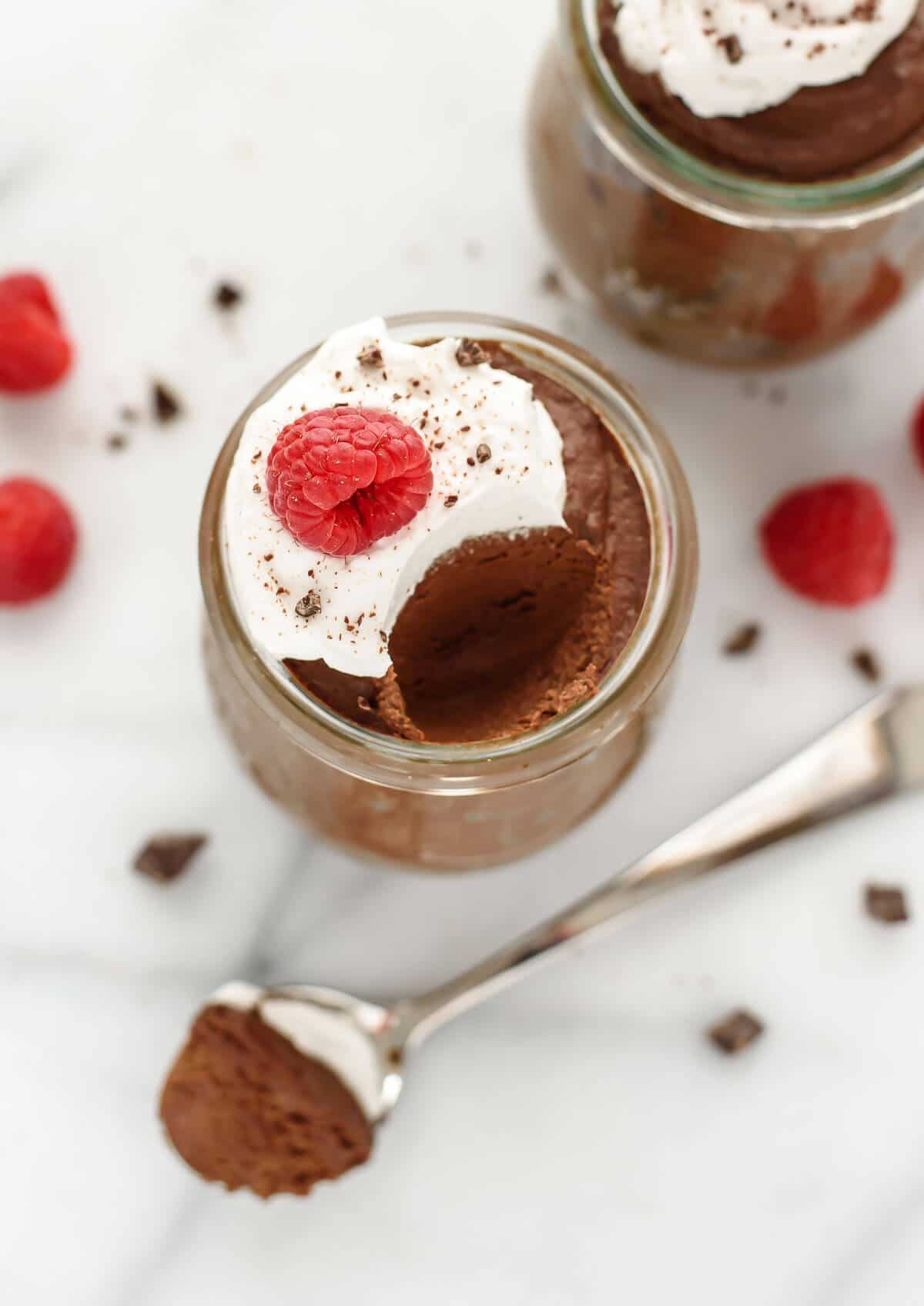 An overhead view of a jar of avocado chocolate mousse with whipped cream and raspberry on top.