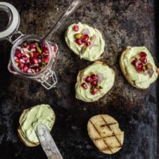 Overhead photo of five avocado toasts with pomegranate seeds on top.