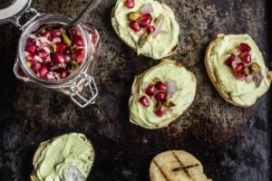 Overhead photo of five avocado toasts with pomegranate seeds on top.