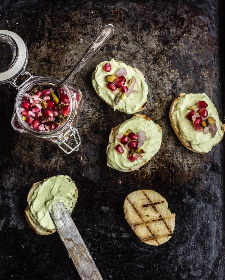 Overhead photo of five avocado toasts with pomegranate seeds on top.