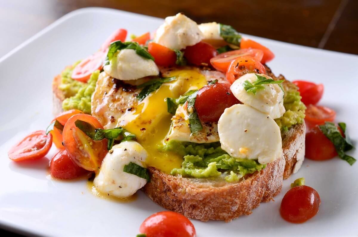 A white plate with avocado toast with caprese. 