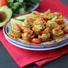 A plate with multiple cauliflower mini muffins topped with guac and sliced tomatoes.