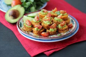 A plate with multiple cauliflower mini muffins topped with guac and sliced tomatoes.
