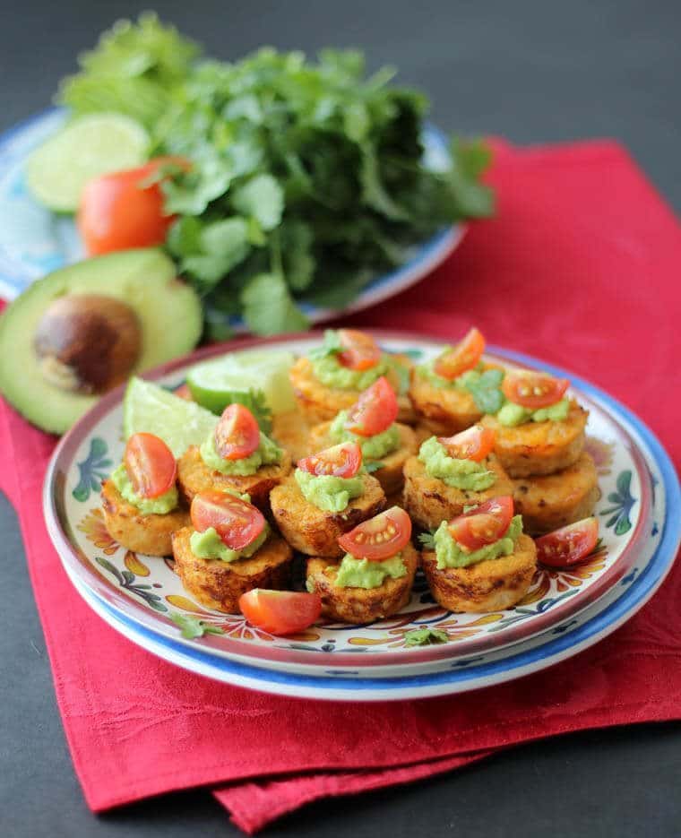 A plate with multiple Mexican cauliflower mini muffins topped with guac and tomatoes.