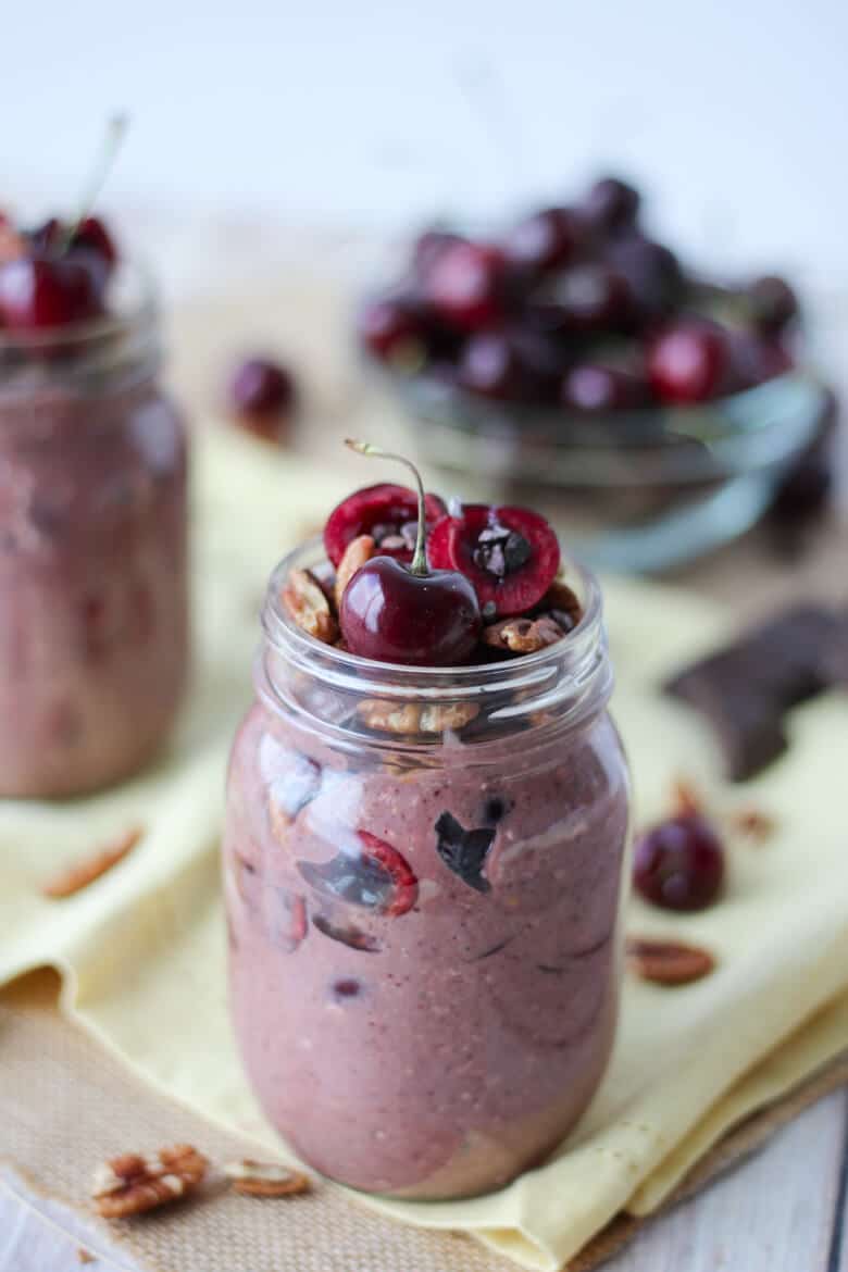 close up of vegan and gluten free cherry cobbler overnight oats in glass jars topped with cherries