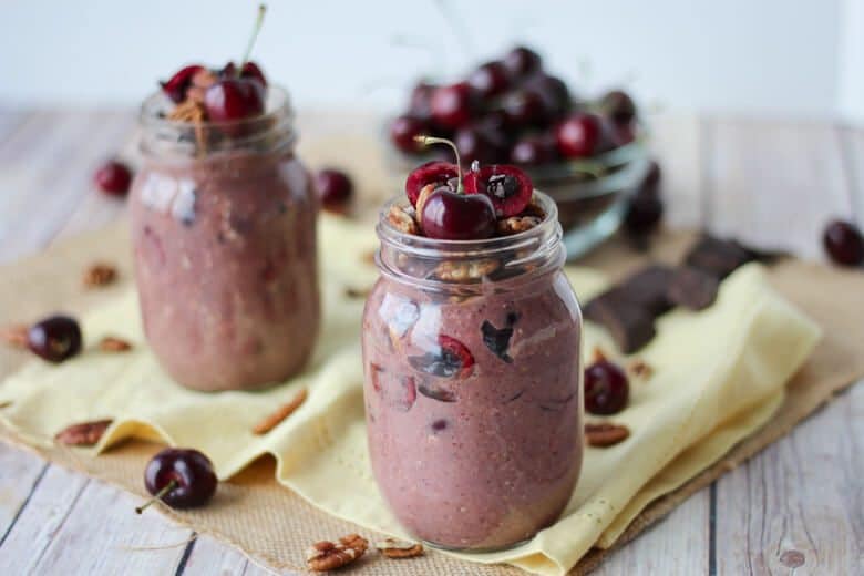 two clear jars filled with cherry cobbler overnight oats garnished with fresh cherries