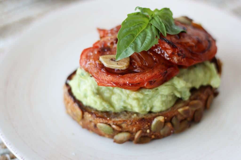 A close up of avocado toast with a tomato on top and basil.