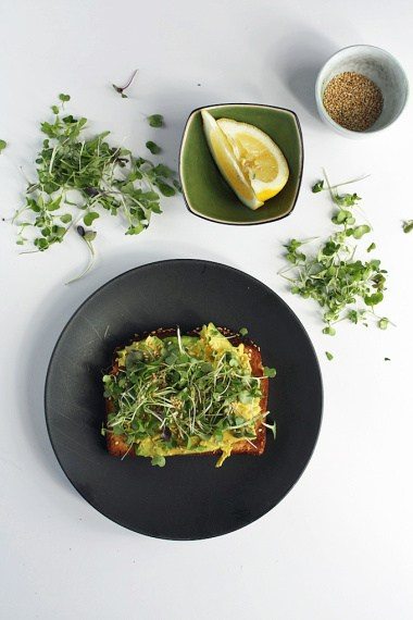 A black plate with an avocado toast and greens on top.