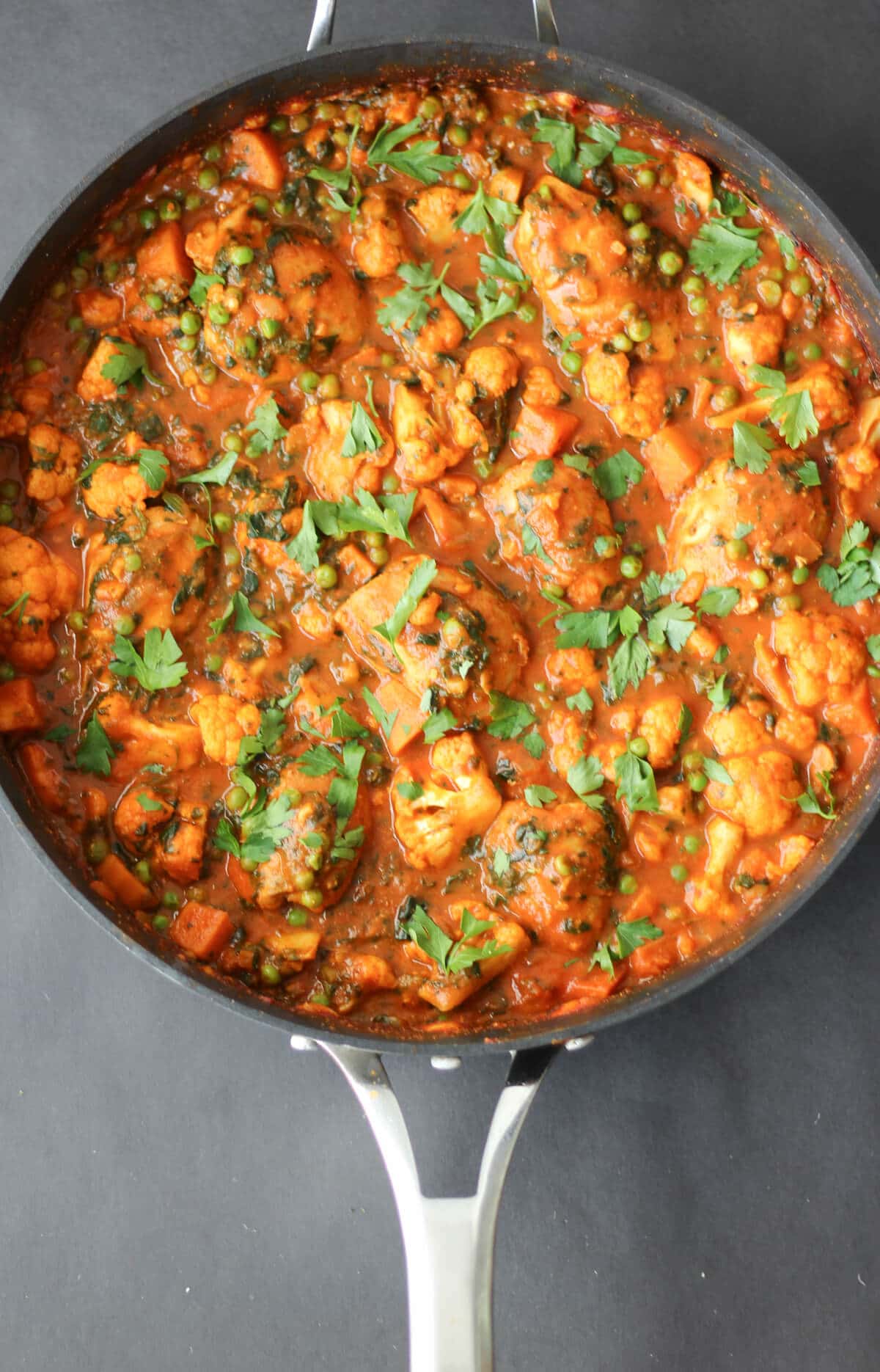 A skillet with chicken curry with garnish on top.