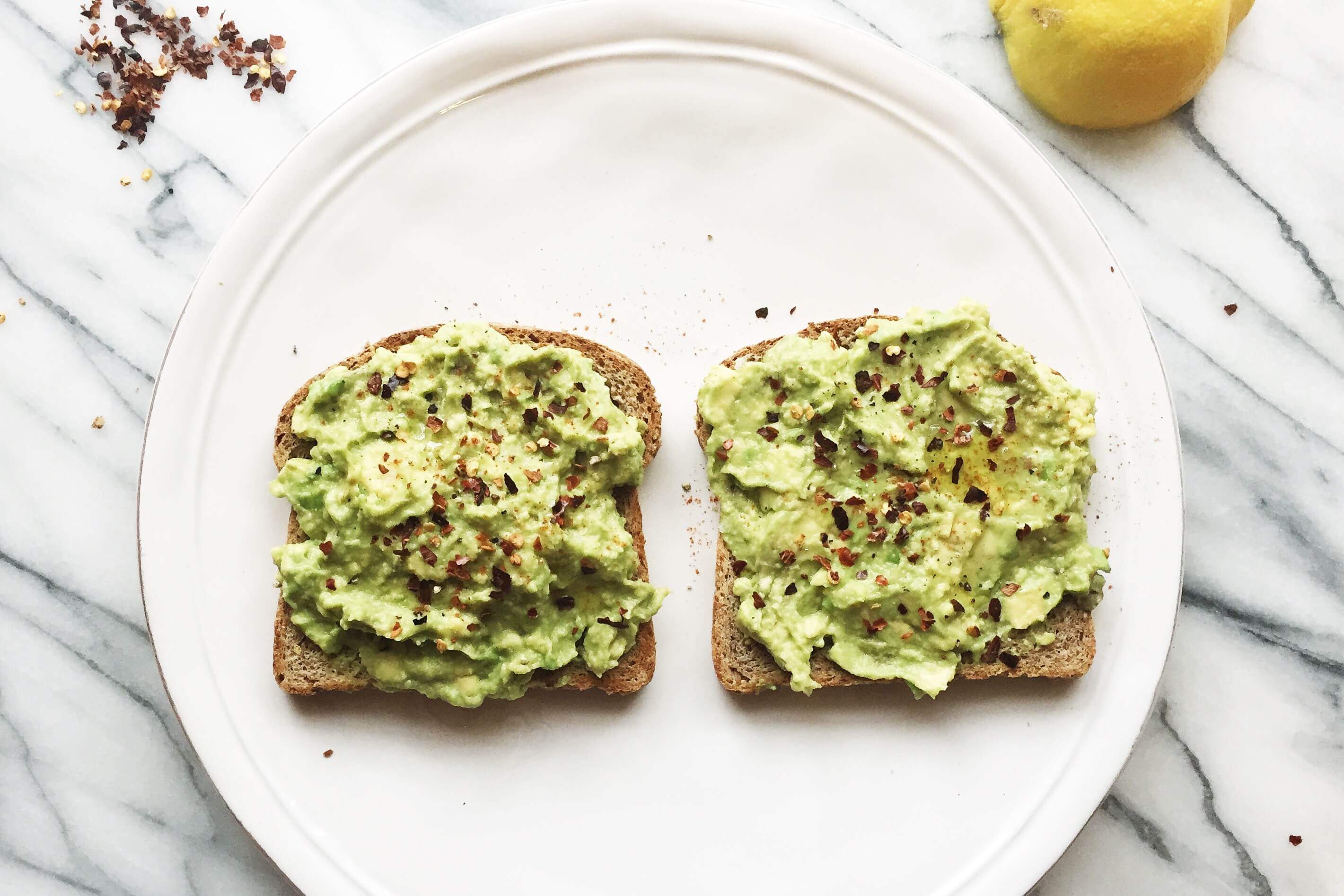 Avocado toast on a white plate with red chili flakes on top.