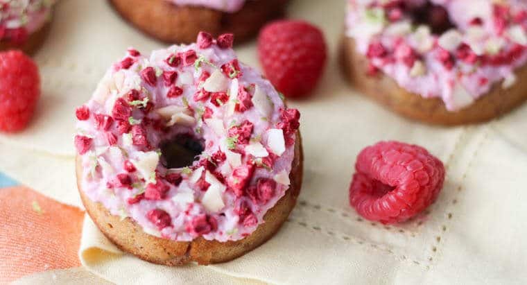 A close up of a raspberry margarita donut with raspberries around.
