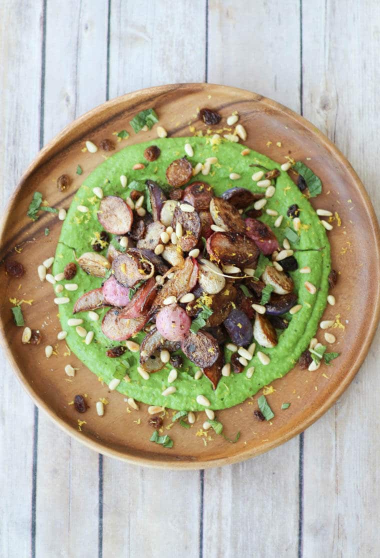 An overhead photo of a brown plate with za\'atar roasted radishes over top of a pea puree with raisins and pine nuts.