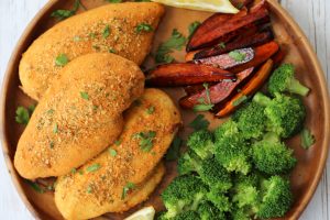 An overhead photo of a brown plate with shake and bake chicken breasts with broccoli florets and vegetable fries.