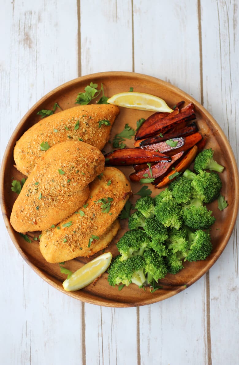 An overhead photo of a brown plate with shake and bake chicken breasts with broccoli florets and vegetable fries.