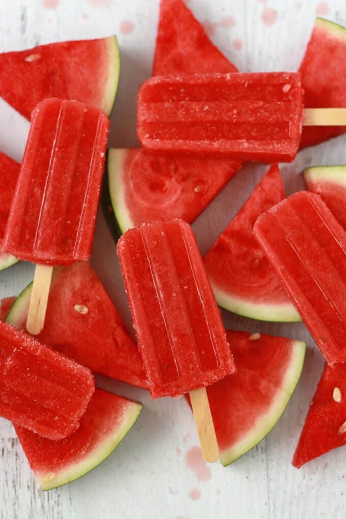 Multiple strawberry watermelon popsicles on top of watermelon slices.