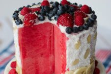 A sliced opened watermelon cake with berries on top.