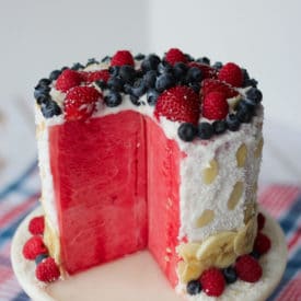 A sliced opened watermelon cake with berries on top.