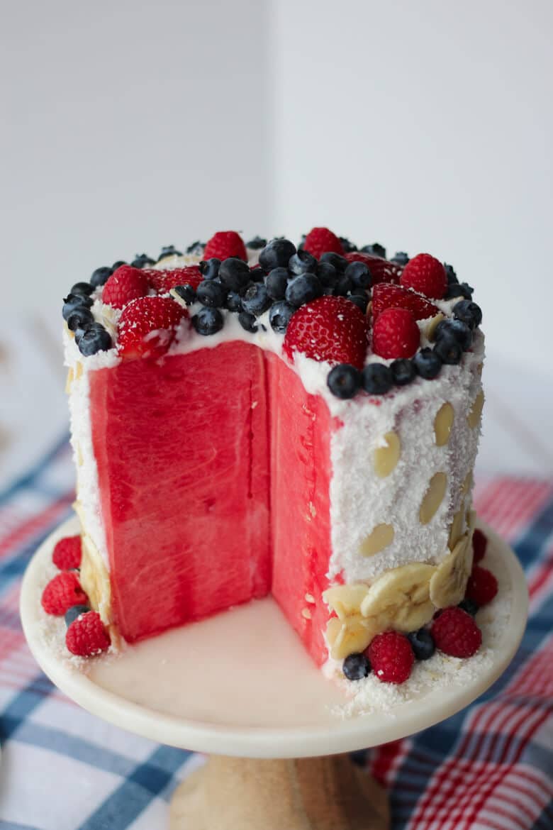 A sliced opened watermelon cake with berries on top.