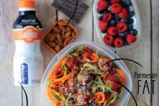 A packed lunch with snacks (mixed fruit, chocolate, almonds) with a bottle of milk beside it.