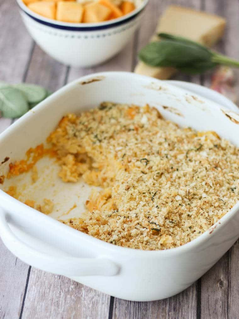 Butternut mac and cheese in a white casserole dish garnished with sage.