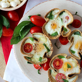 Birds eye view image of veggie egg muffins with tomatoes and basil on a plate.