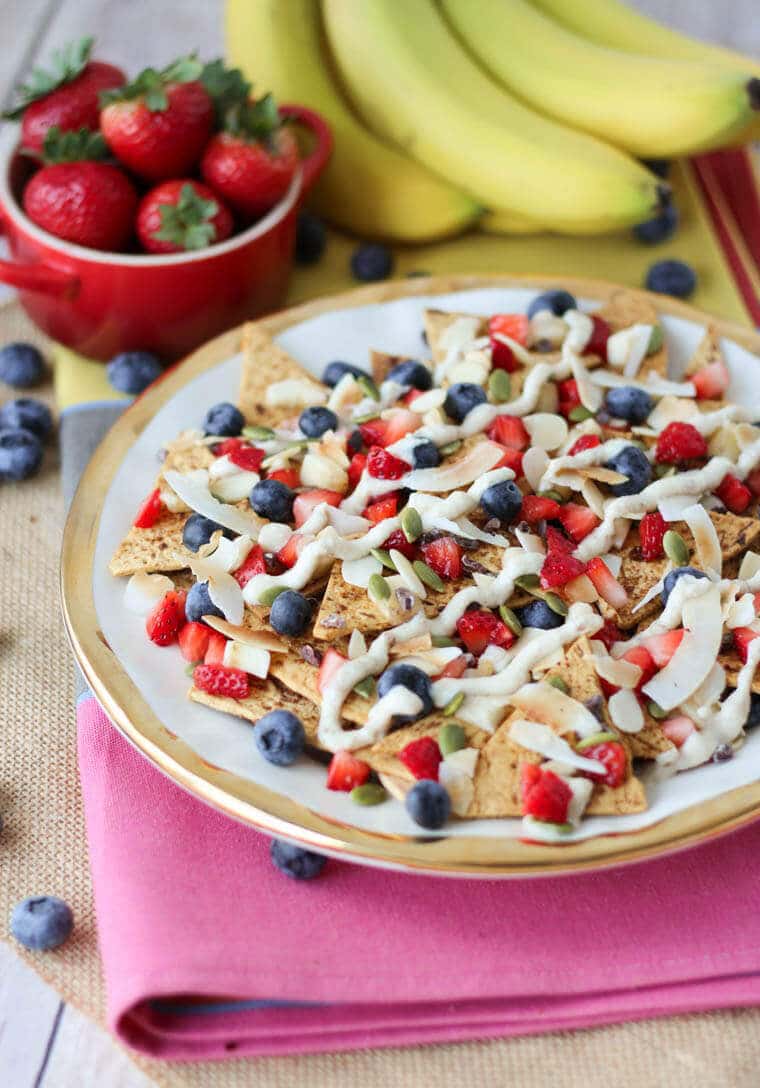 A plate of nachos with fruit on top.