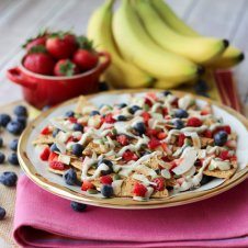 A plate of cheesecake dessert nachos with fruit in the background.