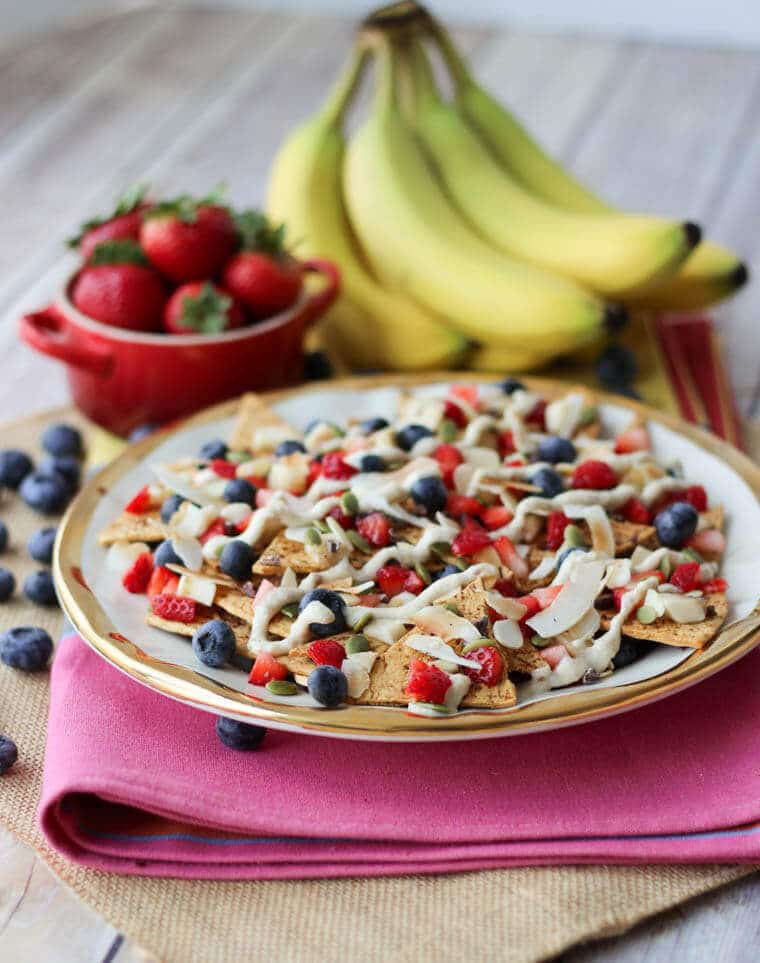 A plate of cheesecake dessert nachos with fruit in the background. 