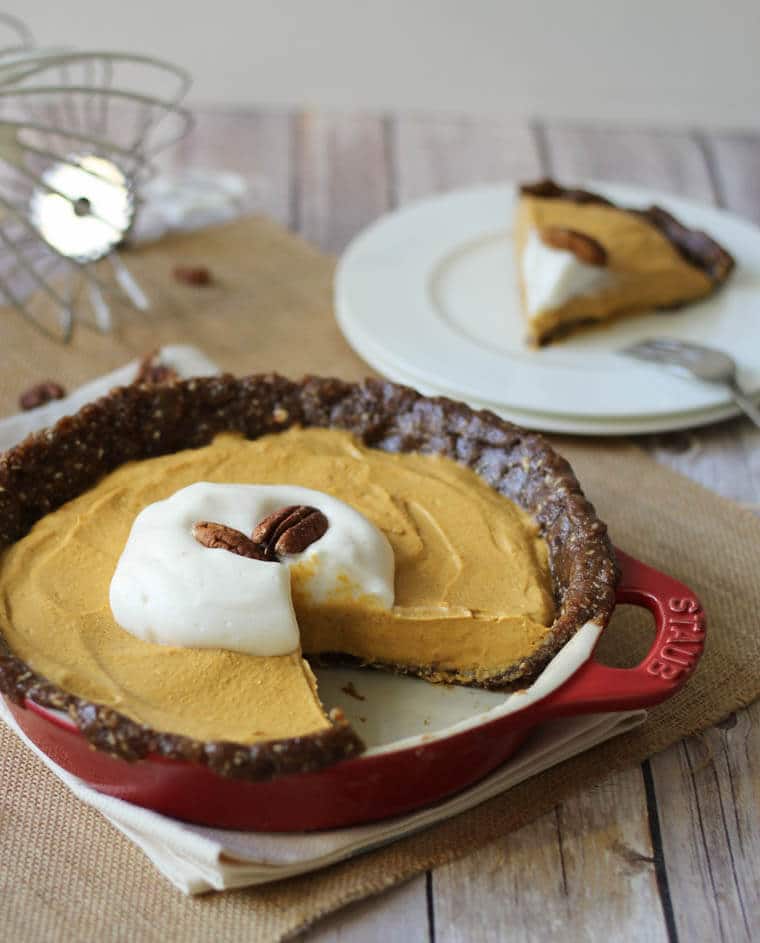 A gluten free pumpkin pie in a red baking dish with a slice cut out onto a plate.