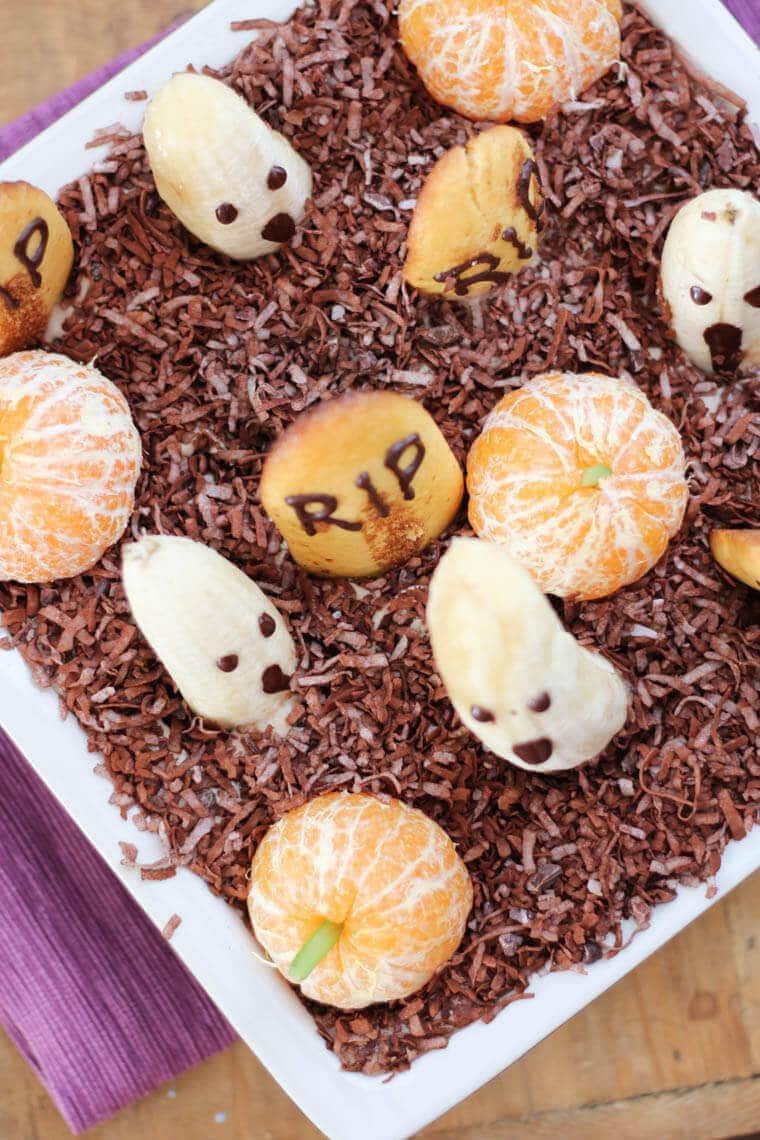 An overhead shot of an edible graveyard made with bananas with ghost faces, lady fingers graves, and clementine pumpkins.