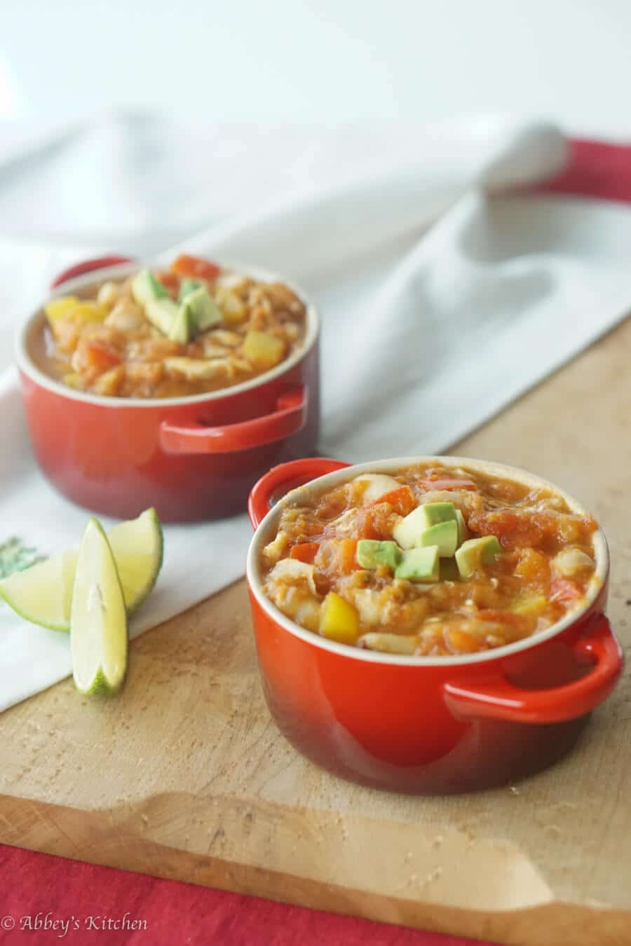 two red ramekins containing turkey pumpkin chilli garnished with avocado and lime