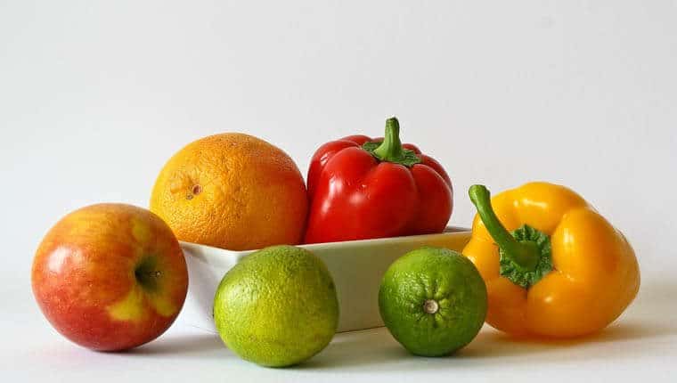 A bowl with bell peppers and oranges with limes around it.