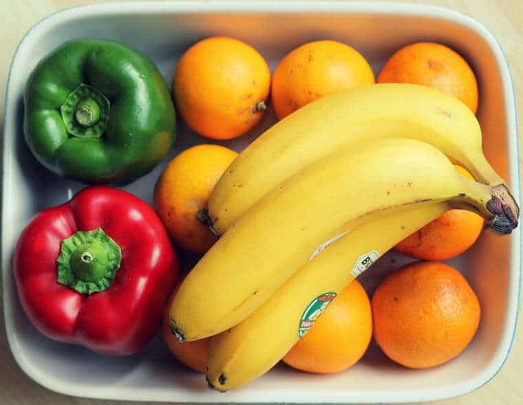 A white dish with bell peppers, oranges, and bananas.