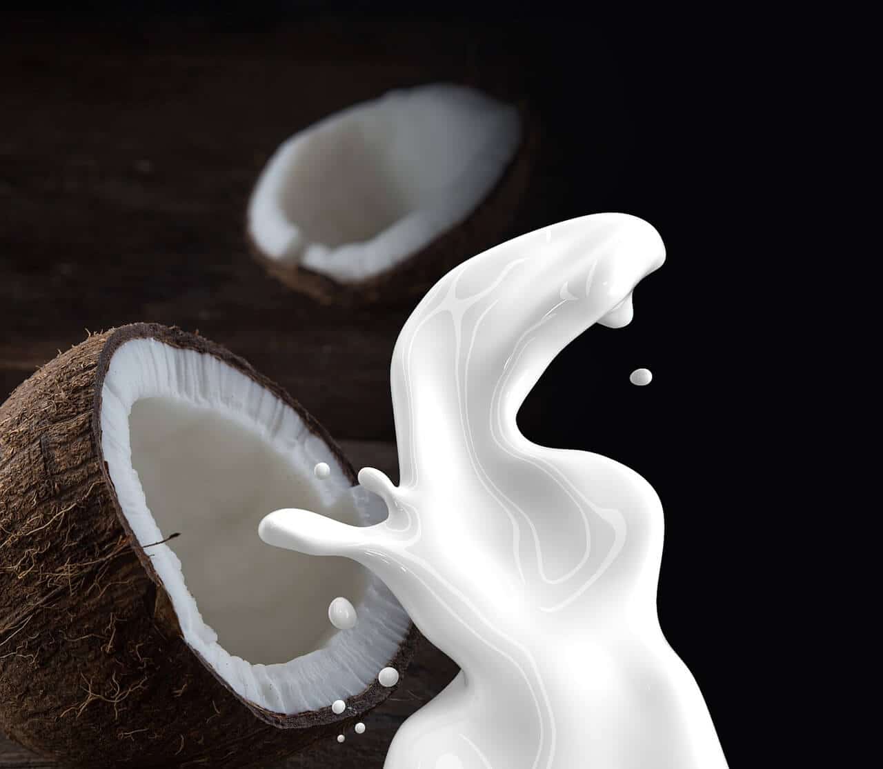 Opened coconuts with a splash of milk in front.