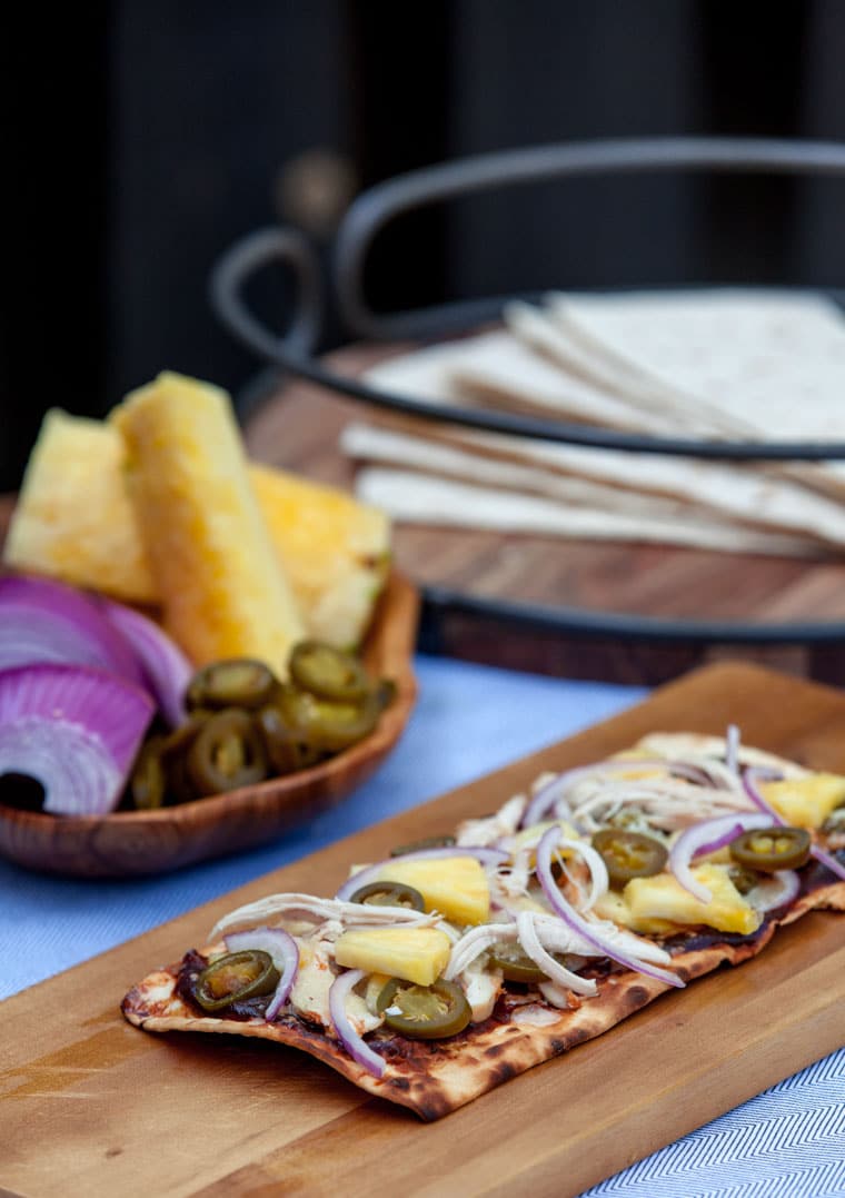 A photo of a grilled pizza using flat bread topped with pineapple, onions, and jalapeno. 