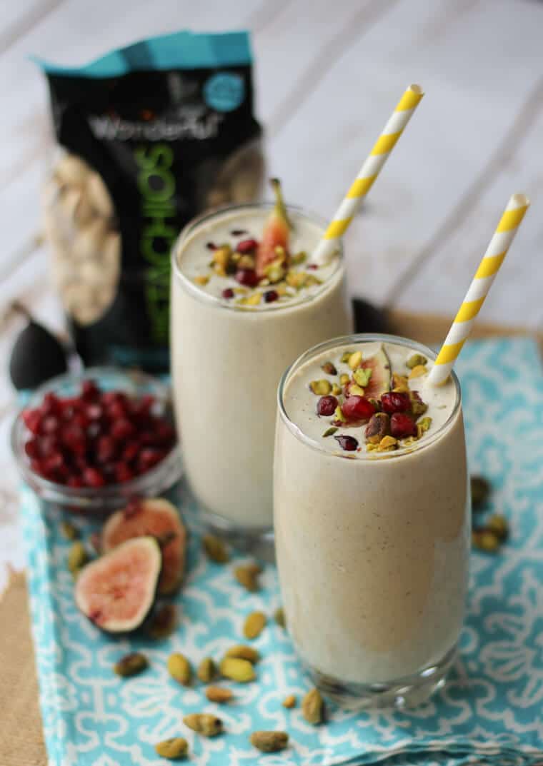 Two glasses of pistachio and tahini protein smoothie with a yellow straw in each glass.