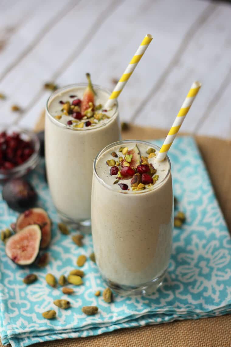 Two glasses of post workout smoothie with pistachio and tahini with a yellow straw in each glass.