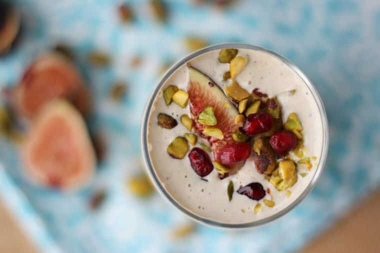 An overhead image of a glass of smoothie that is topped with pistachio, pomegranate seeds, and fig.