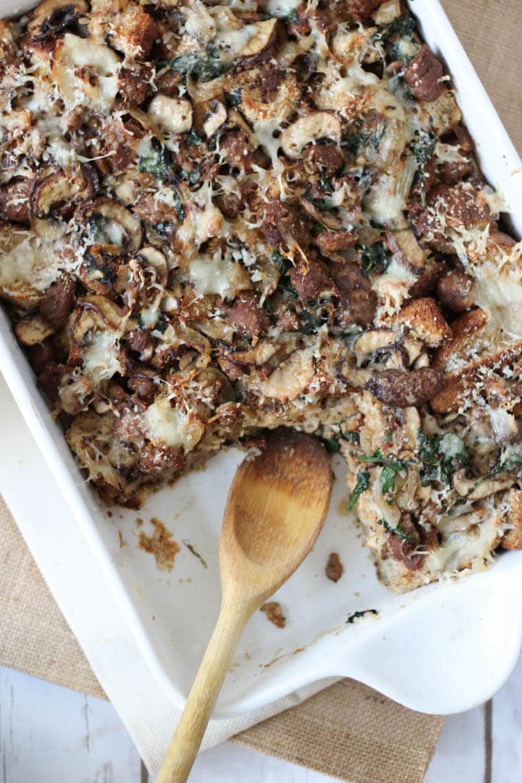 Overhead photo of a white baking dish containing sausage strata with a wooden spoon inside.