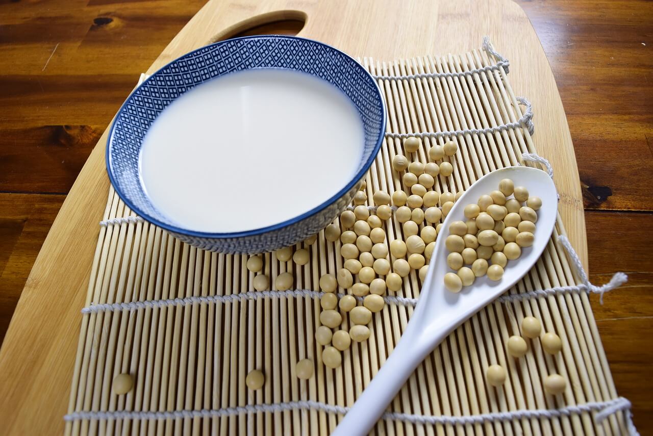 A bowl of soy milk with soy beans around it.