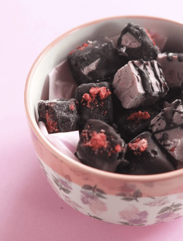 A bowl of chocolate covered strawberry cheesecake bites.
