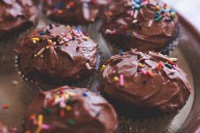 A close up of multiple chocolate cupcakes with rainbow sprinkles on top.