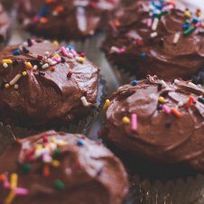 A close up of multiple chocolate cupcakes with rainbow sprinkles on top.