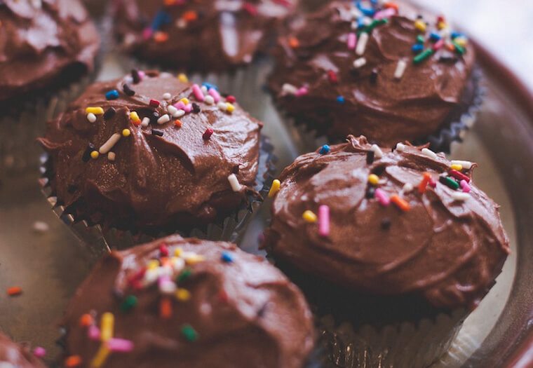 A close up of multiple chocolate cupcakes with rainbow sprinkles on top.