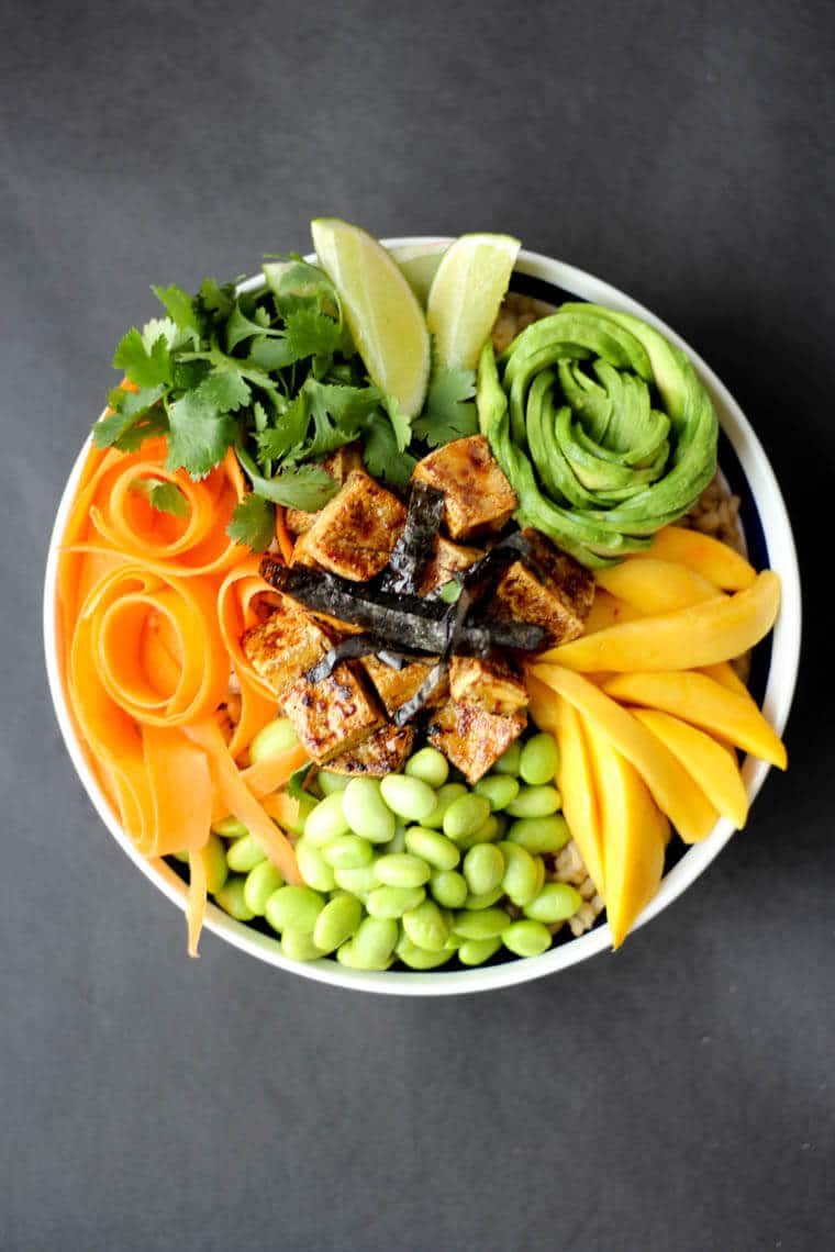 An overhead image of a poke bowl with crispy tofu, carrots, avocado, beans, lime, and cilantro.