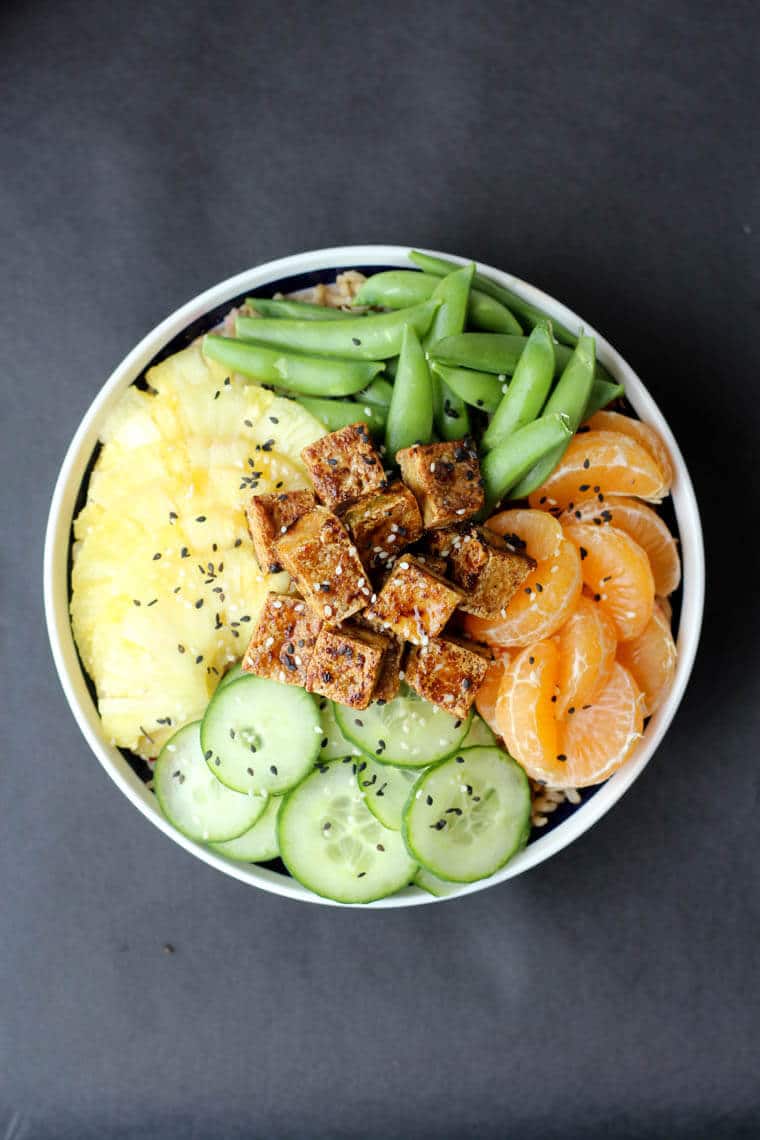 An overhead image of a poke bowl with crispy tofu, clementines, cucumbers, snap peas.   