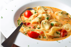 A bowl of tomato and tortellini soup.