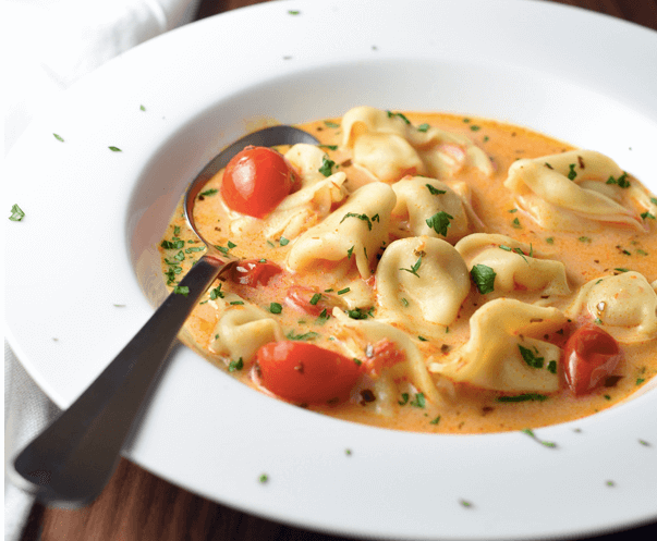 A bowl of tomato and tortellini soup.