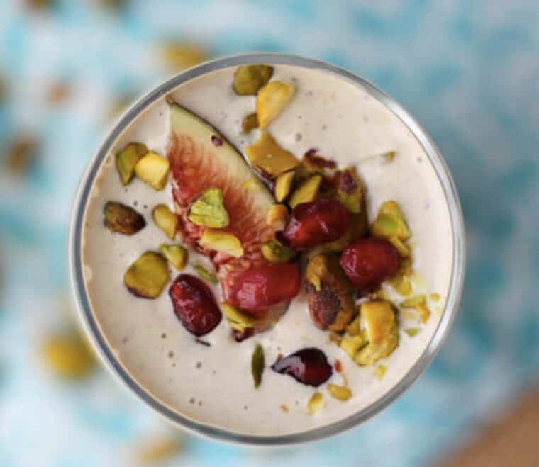 birds eye view of pistachio tahini smoothie in a clear glass garnished with fruit and pistachios