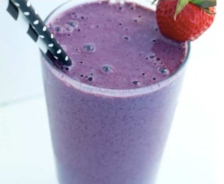 A cup of smoothie that is purple with a strawberry on top.